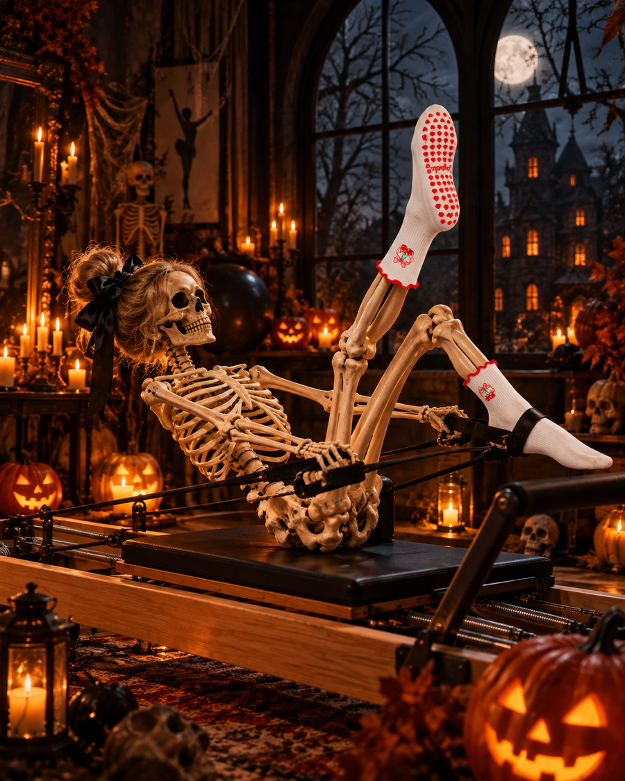 Skeleton doing Pilates on a reformer in Gripbelle Cherry Ruffle grip socks, Halloween studio